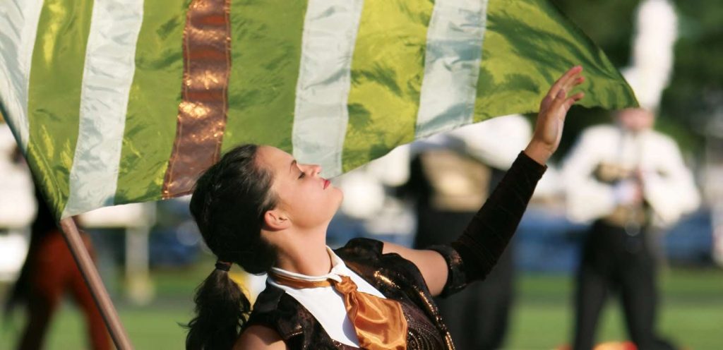 color guard member in a brown and cream uniform swinging a green striped flag