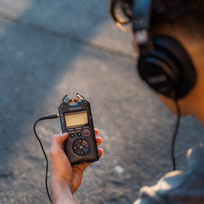 tacsam handheld audio recorder dr40x held in hand attached to headphones on persons ears